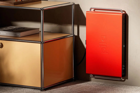 A red Pila Mesh Home Battery mounted on the wall beside a credenza, its display showing 5 days 6 hours of backup