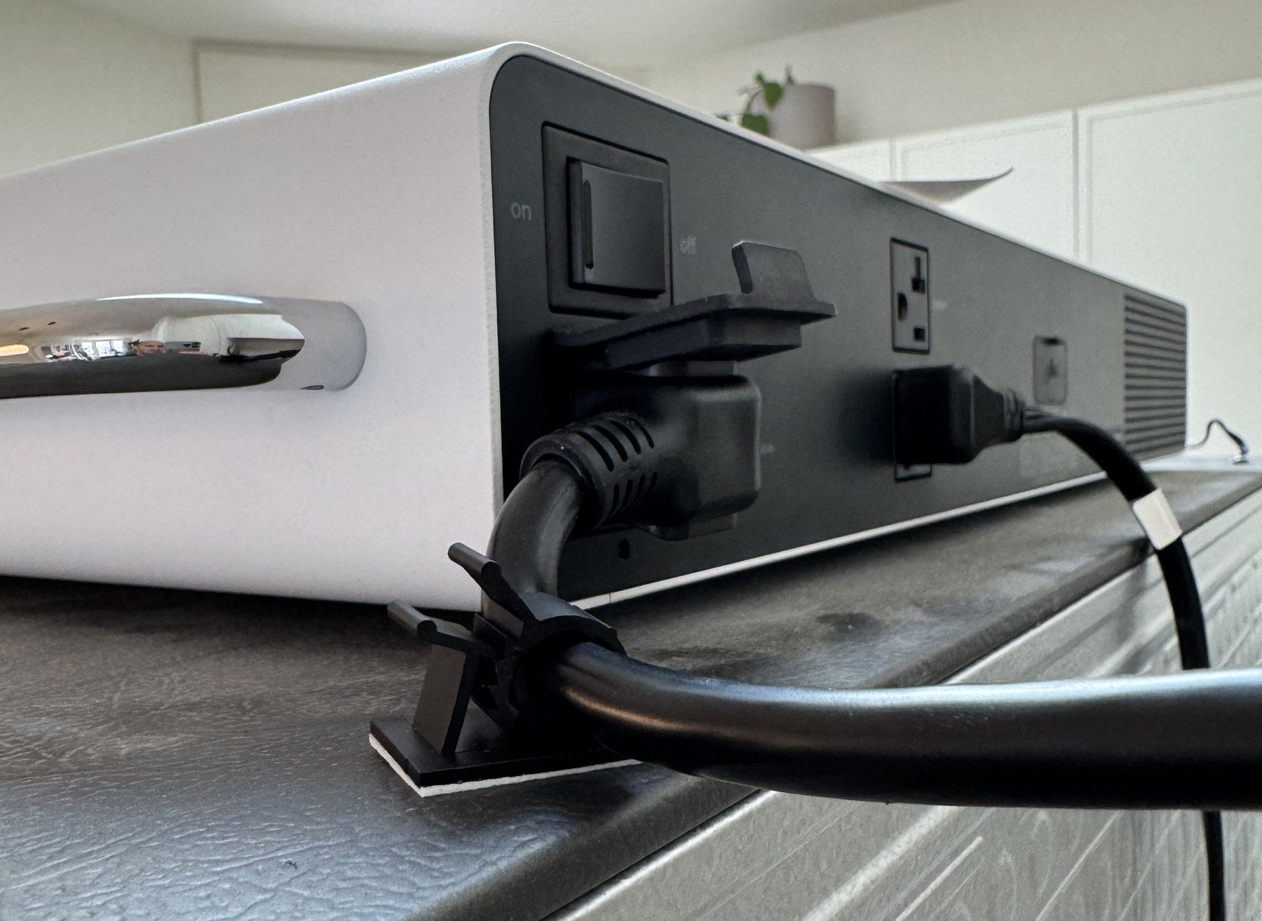 A cable clip stuck to the top of the fridge holding the cord that runs to the outlet on the back of a Pila